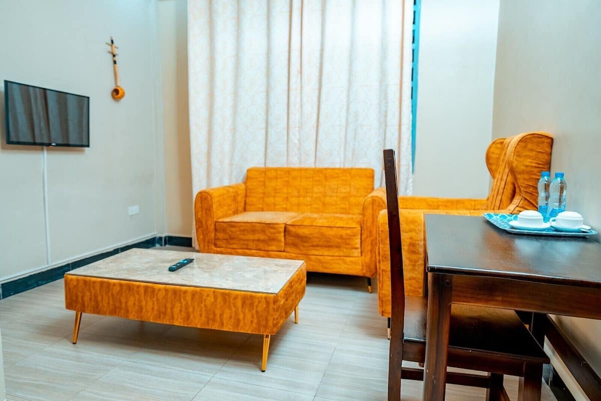 A living room with a sofa, a coffee table, a TV, and a dining table with water bottles.
