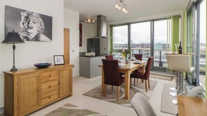 A modern apartment with a dining area, kitchen, and large windows offering city views. - The Penthouse, Phoenix Quay (Plymouth)