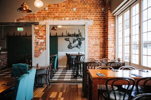 A restaurant interior with brick walls, wooden flooring, and a cow mural. Tables and chairs are arranged for dining. - The Rix Hotel Motel (Charters Towers)