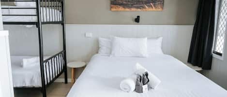 A hotel room with a bunk bed, a single bed, a painting on the wall, and a small round table.