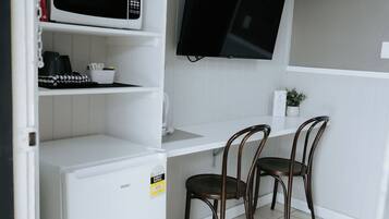 A compact kitchenette with a microwave, a small refrigerator, a flat-screen TV, and two wooden chairs.