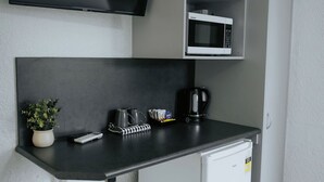 Eine kompakte Küchenzeile mit Flachbildfernseher, Mikrowelle, Kaffeemaschine und einem kleinen Mülleimer.