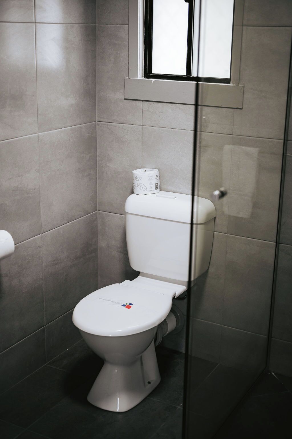 A modern bathroom with a toilet, a toilet paper holder, and a glass shower enclosure.