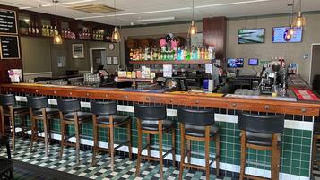 A bar with a checkered floor, bar stools, and a variety of bottles and glasses on shelves.