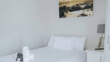 A neatly made bed with white linens, a black headboard, and a small bedside table with a lamp.