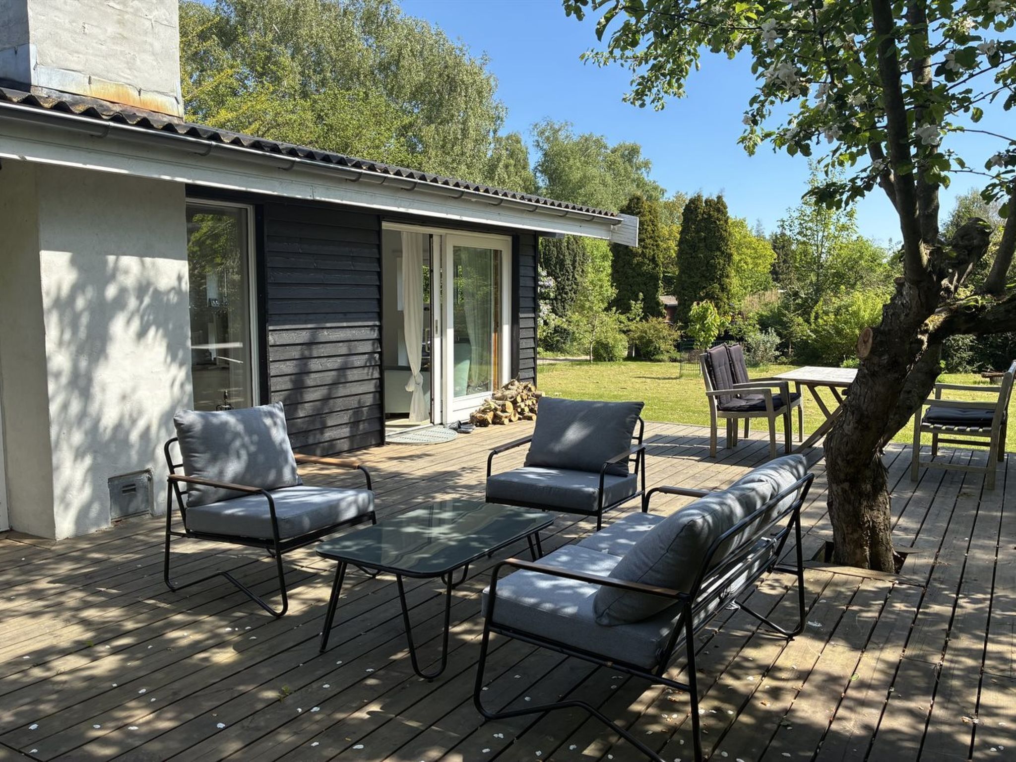 A deck with outdoor furniture, a building with a dark exterior, and a tree.