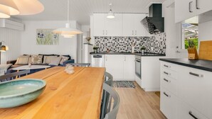 Una cocina moderna con armarios blancos, una mesa de comedor de madera e iluminación colgante.