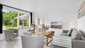 Una sala moderna con un ventanal grande, una mesa de comedor de madera, mobiliario tapizado en gris y un cuadro en la pared.