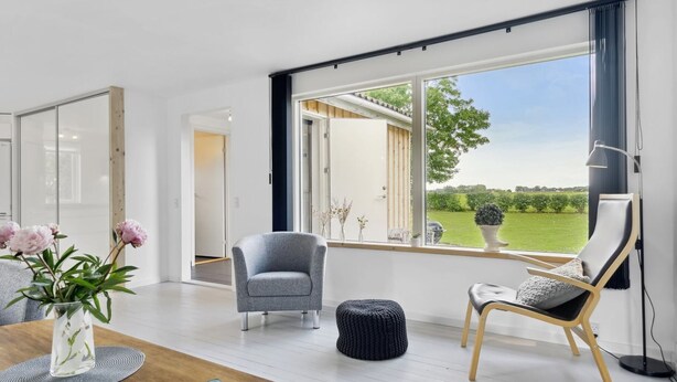Una sala de estar moderna con un ventanal grande, un sillón gris, una mesa de centro de madera y una revista.