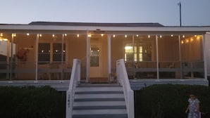 A building with a covered porch, a staircase leading to the entrance, and a vehicle parked nearby. - Private cottage at the end of the road with hot tub, swim mat, kayaks, and a your private dock, 3 miles to the beach. (Cedar Point)
