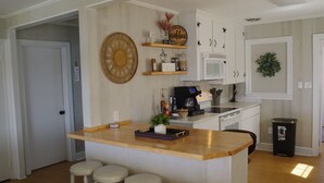 A compact kitchen with a central island, white cabinetry, and a coffee-themed decor. - Private cottage at the end of the road with hot tub, swim mat, kayaks, and a your private dock, 3 miles to the beach. (Cedar Point)