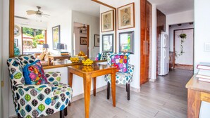 A dining area with a wooden table and two patterned chairs, a ceiling fan, and framed artwork on the walls.