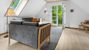 A modern loft bedroom with a sloped ceiling, a skylight, a grey sofa, a wooden floor, and a view of greenery outside. - "Rina" - 250m from the sea by Interhome (Hasle)