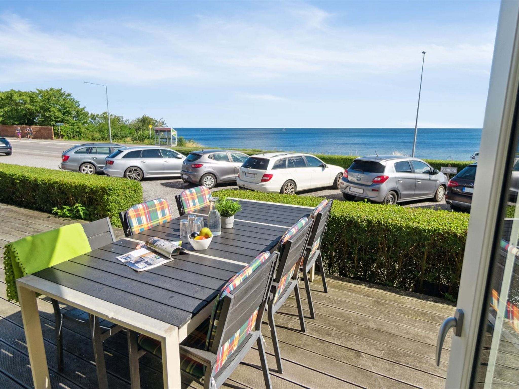 Terraza con mesa y sillas, con vistas a un aparcamiento y al mar.