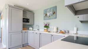 Une cuisine moderne avec des meubles gris, un plan de travail blanc, un four à micro-ondes, un évier et un tableau représentant des canards accroché au mur.