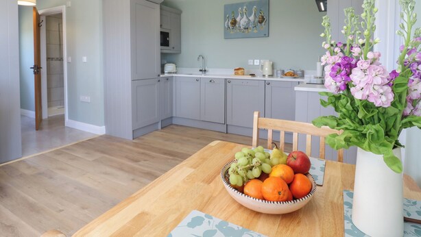 Une cuisine moderne avec des meubles gris, une table à manger agrémentée d’un panier de fruits et un vase rempli de fleurs.