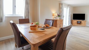 Een eethoek met een houten tafel, stoelen en een televisie op de achtergrond.