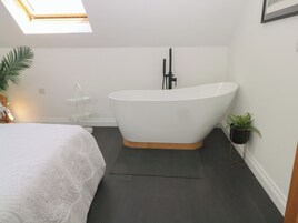Un baño moderno con una bañera independiente, un estante pequeño blanco y una planta en maceta.