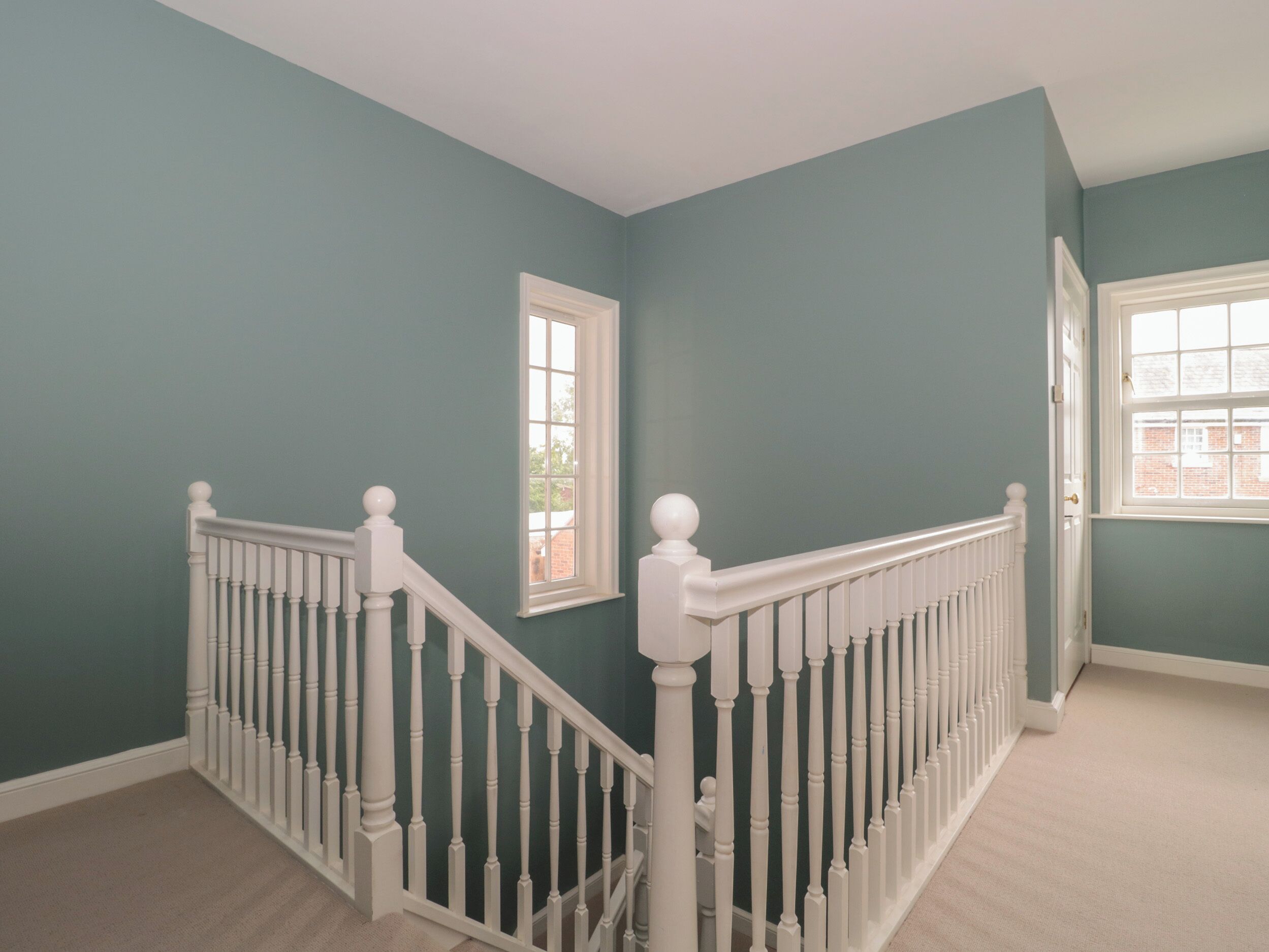 Una escalera con balaustres blancos y una alfombra beige.