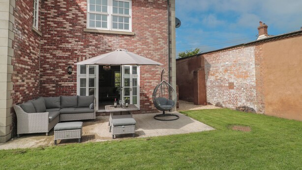 Une maison en briques dotée d’un patio comprenant un canapé, un fauteuil suspendu et une table avec deux bouteilles.