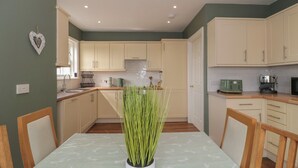 Une cuisine avec des meubles de couleur claire, une table à manger avec des chaises et une plante en pot placée au centre.