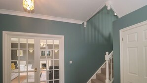 Un couloir avec un escalier, une porte dotée de panneaux de verre et un luminaire au plafond.