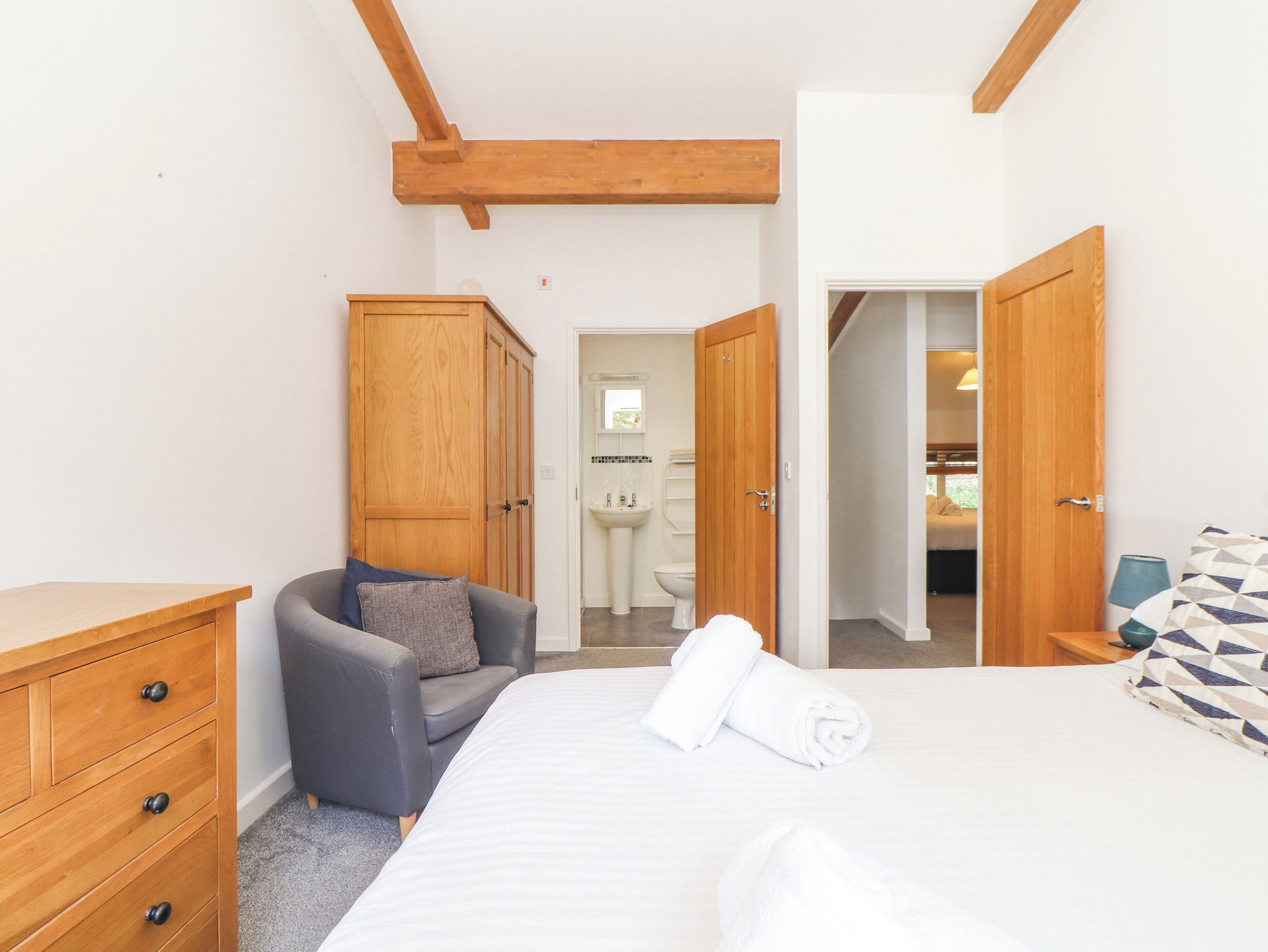 Une chambre à coucher comprenant un lit, une commode en bois, un fauteuil gris et une armoire.