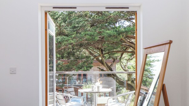 Un dormitorio con un gran ventanal corredera que da a un balcón exterior con una mesa y sillas.
