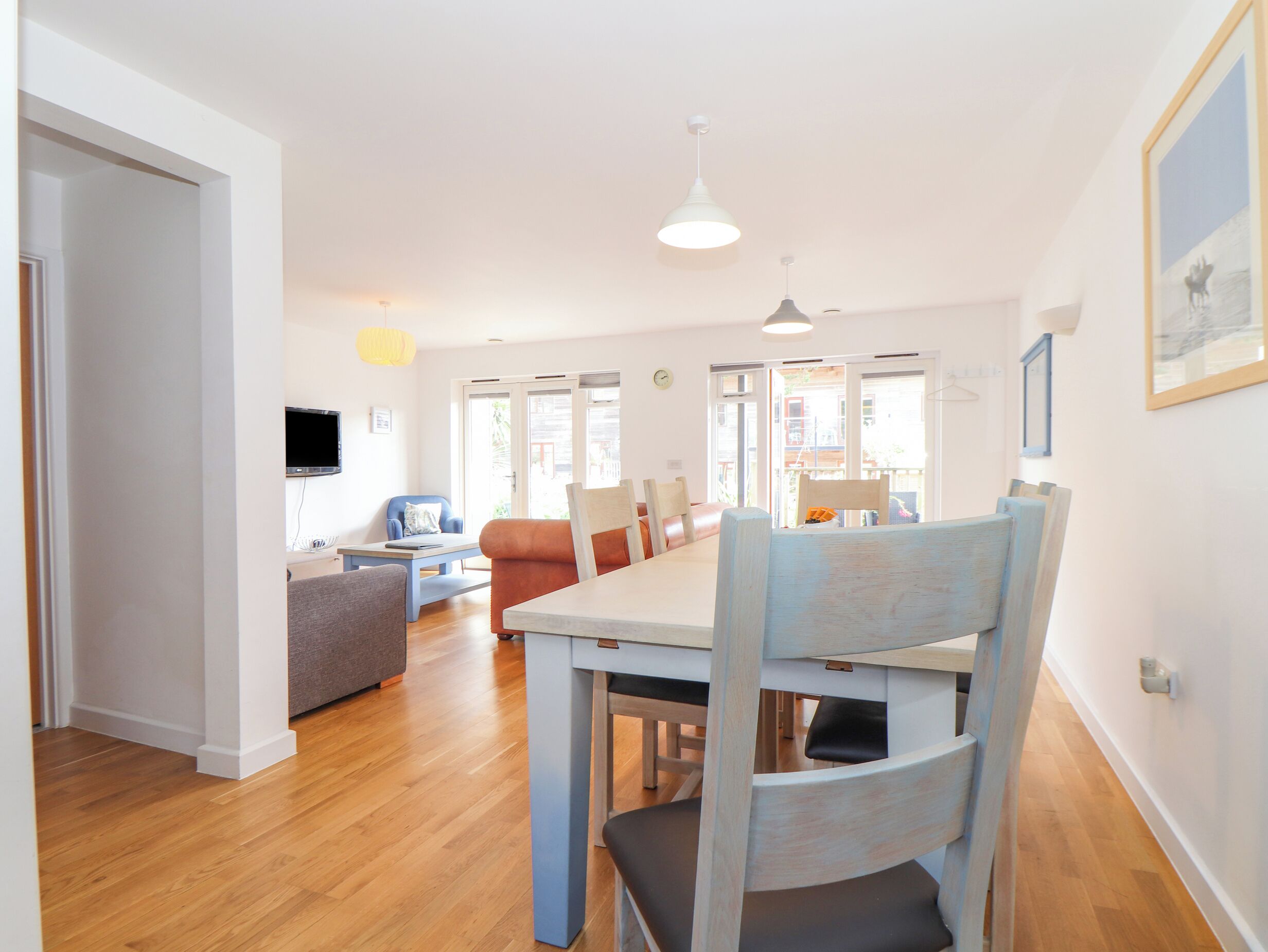 A modern dining area with a wooden table and chairs, a sofa, and a television.