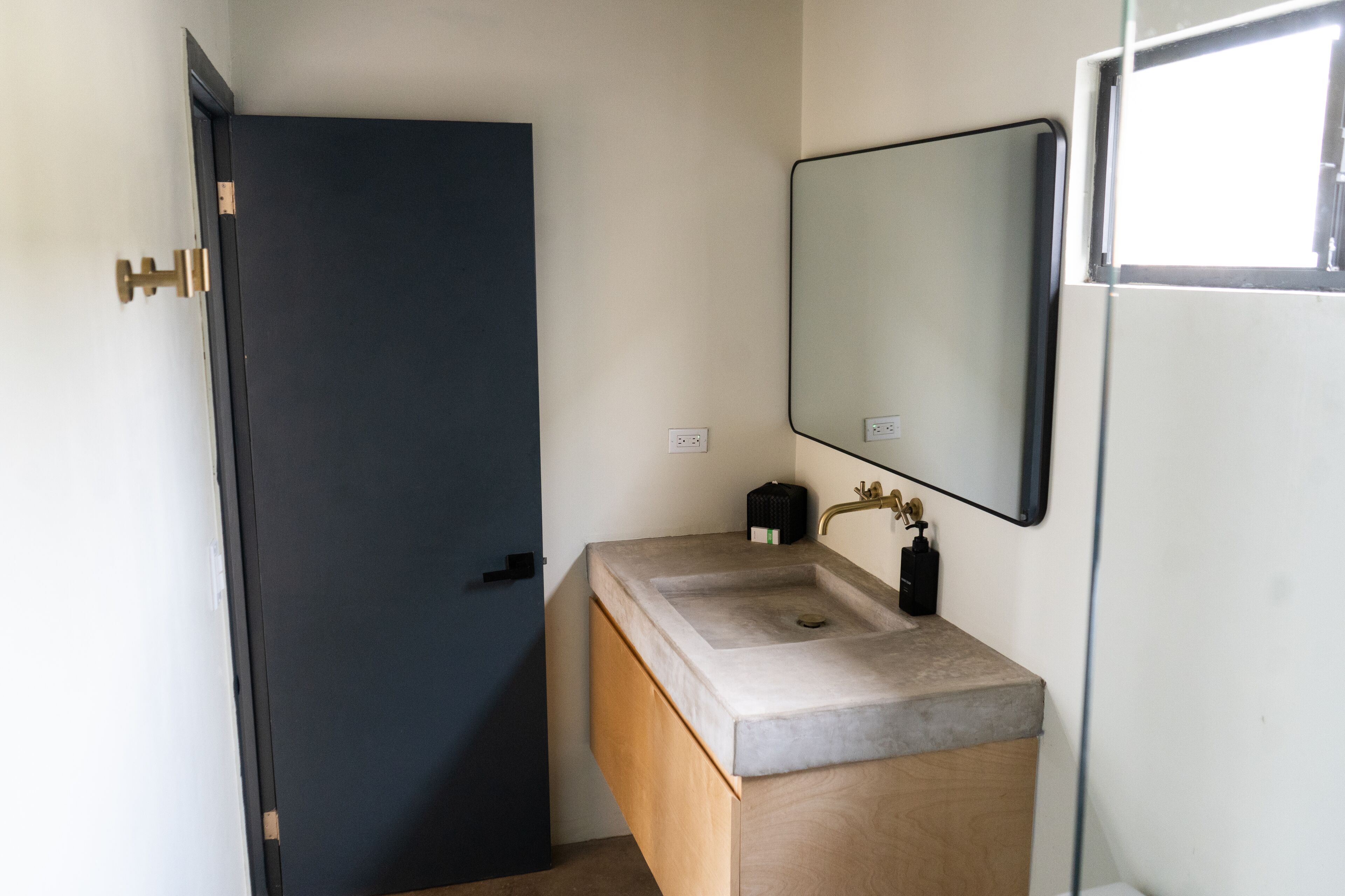 A bathroom with a dark door, a sink with a mirror, and a small window.