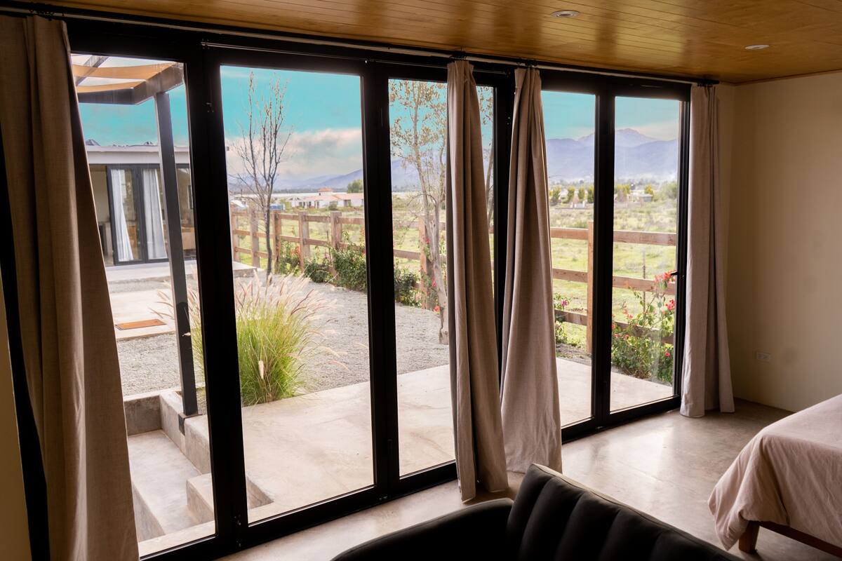 A room with large sliding glass doors leading to a patio with a wooden fence, steps, and a view of a mountainous landscape.