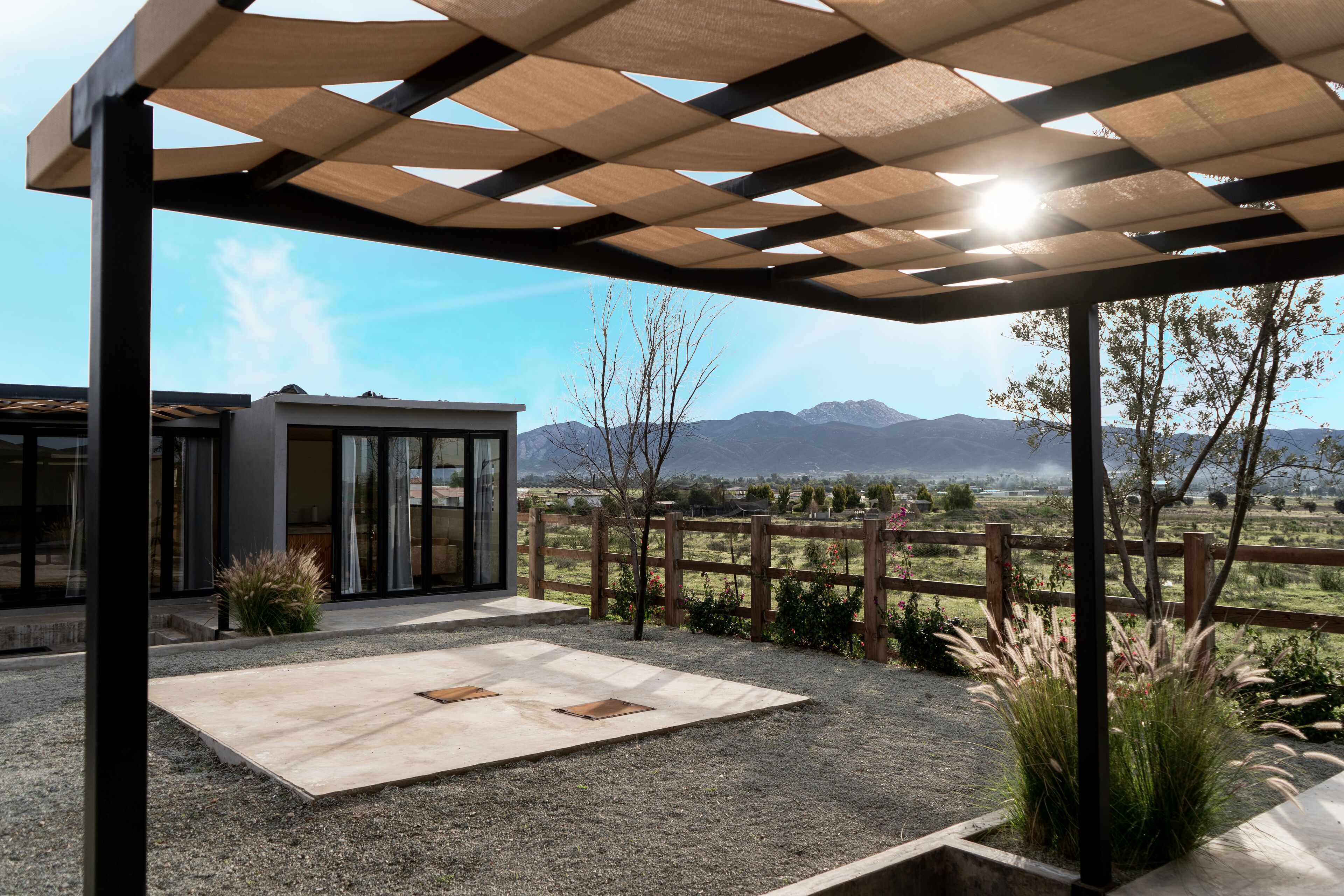 Un espace extérieur abrité offrant une vue sur les montagnes, avec une clôture en bois et une terrasse en gravier.