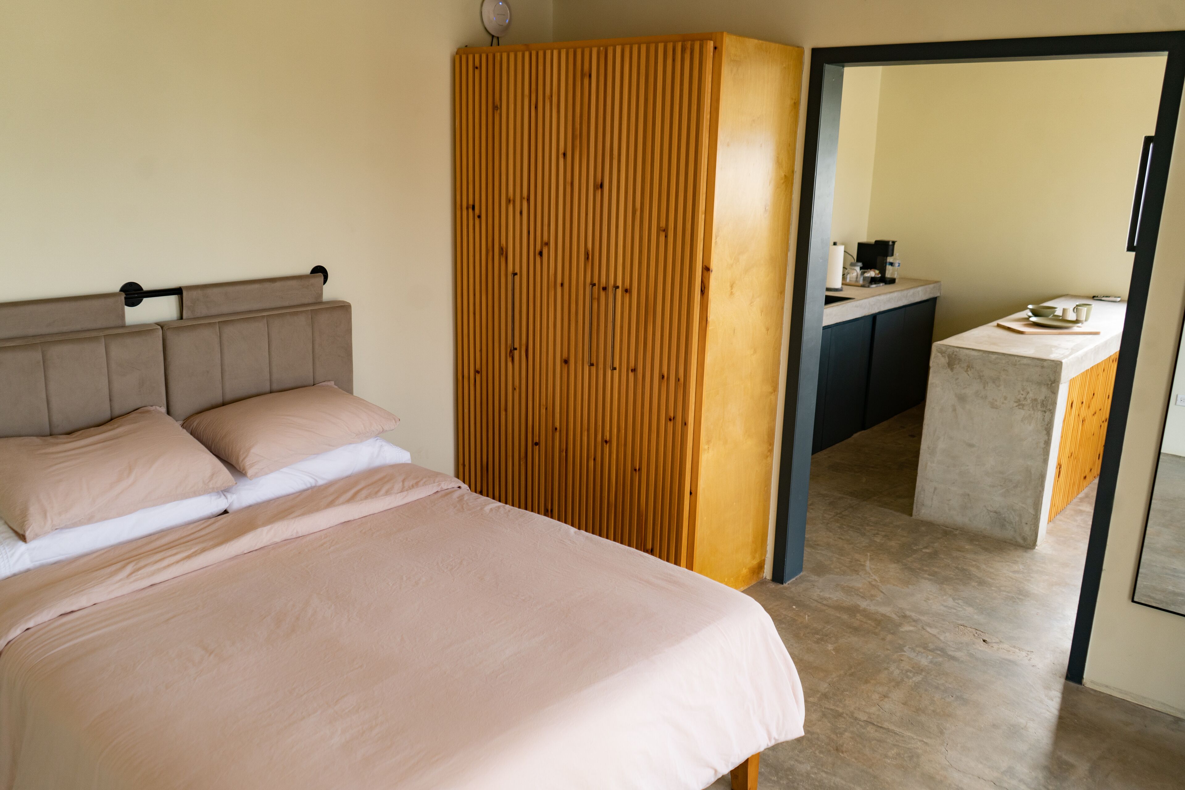 A bedroom with a bed, a wooden wardrobe, and a kitchenette area.