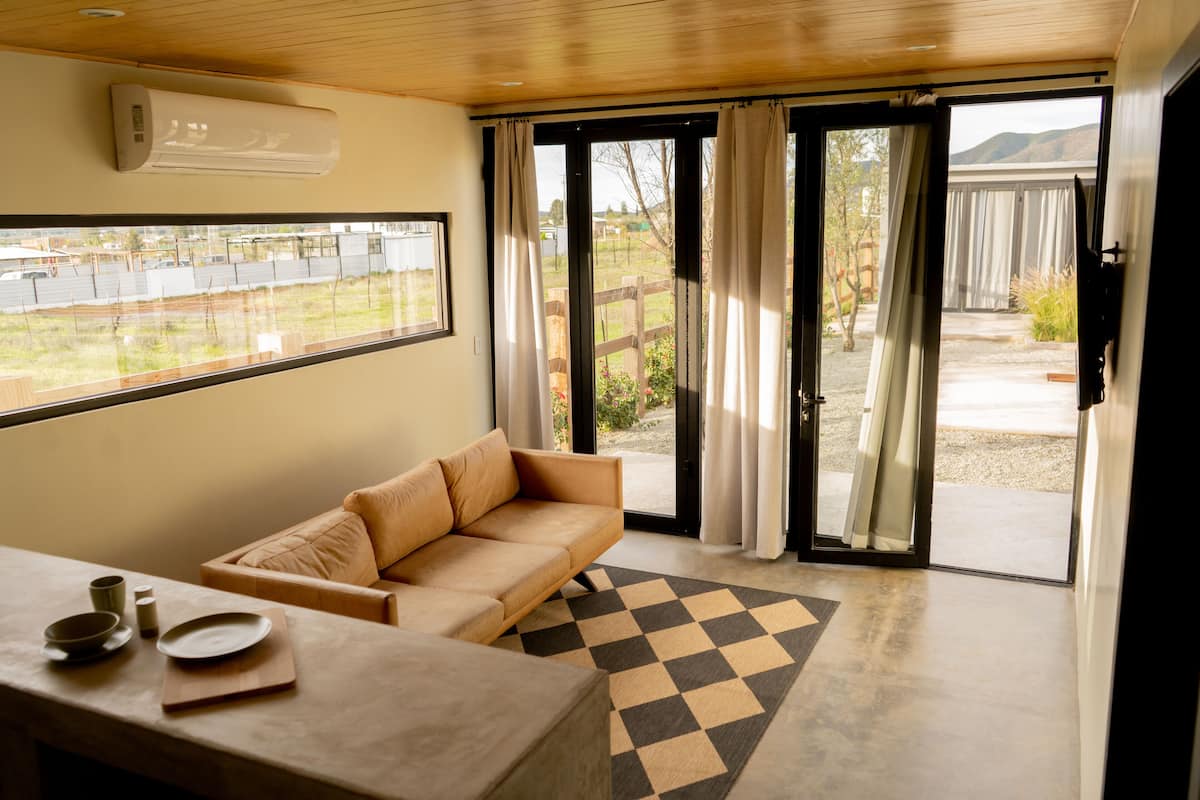 A modern room with a beige sofa, a dining table with plates and bowls, and a checkered rug.