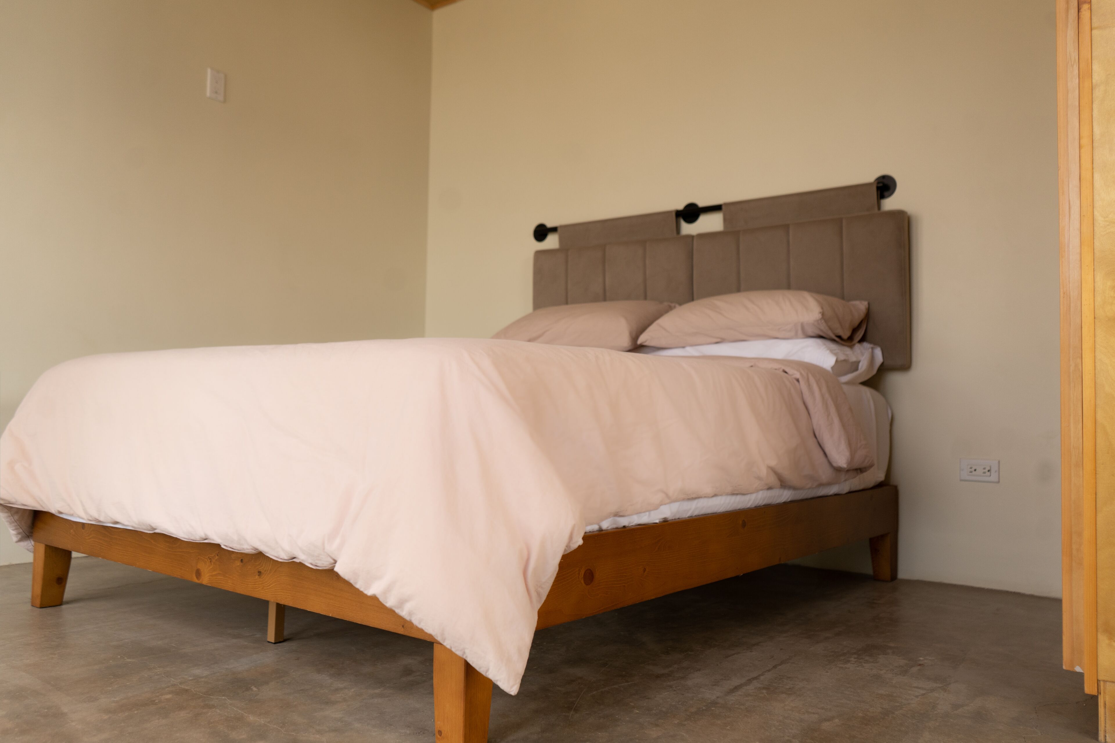 Ein Einzelbett mit Holzrahmen und Kopfteil, eine beige Wand und ein Holzboden.
