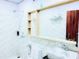 Un baño moderno con paredes de mármol, un mueble de tocador de madera, un espejo grande y una zona de ducha.
