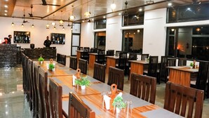 Un comedor amplio con largas mesas y sillas de madera, iluminación colgante y una zona de bar al fondo.