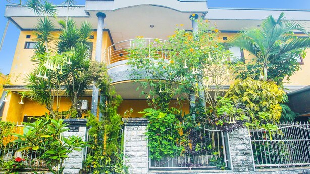 A multi-story building with a curved balcony, surrounded by lush greenery and a stone wall. - SPOT ON 91620 Skypiea Guest House (Tasikmalaya)