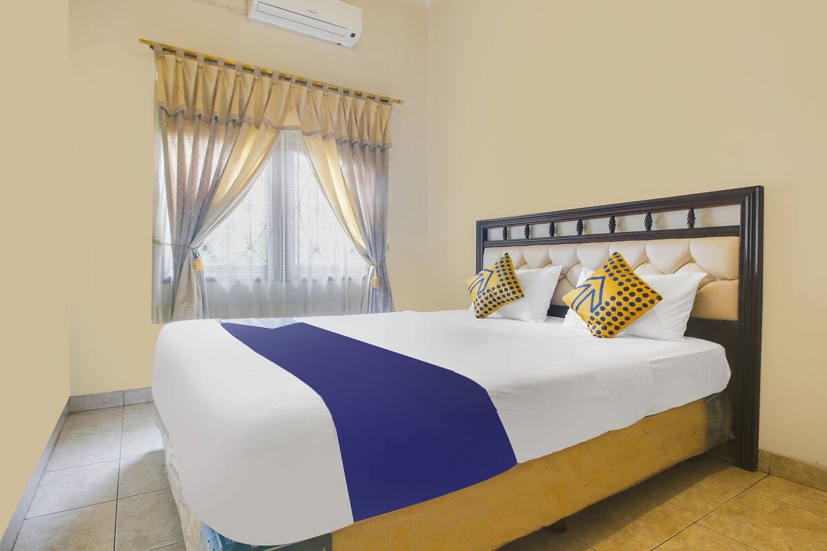 Una cama bien hecha con un detalle azul, un cabecero con un diseño decorativo y una ventana con cortinas.