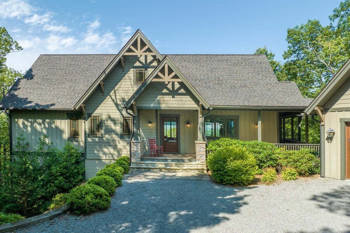 A two-story house with a front porch, stone pillars, and a gravel driveway.