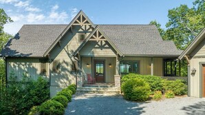 A two-story house with a front porch, stone pillars, and a gravel driveway. - Maple Cottage in Sutton Knob (Pisgah Forest)