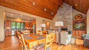 A spacious kitchen with wooden cabinets, a stone fireplace, and a dining area with a wooden table and chairs. - Maple Cottage in Sutton Knob (Pisgah Forest)