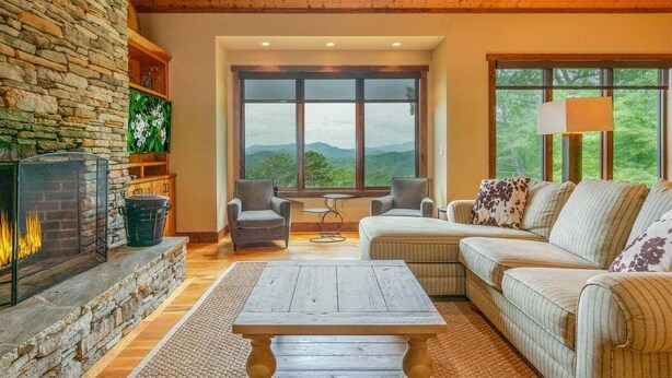 A cozy living room with a stone fireplace, comfortable seating, and a large window offering a scenic view. - Maple Cottage in Sutton Knob (Pisgah Forest)