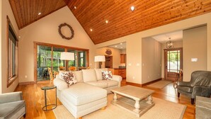 A spacious living room with a wooden ceiling, a sectional sofa, a coffee table, and a leather armchair. - Maple Cottage in Sutton Knob (Pisgah Forest)