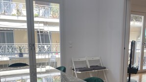 En rummelig stue med et stort marmorbord, grønne stole og en skydedør til en balkon med udsigt over en bygning og et grønt område.