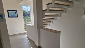 Een modern interieur met een trap, een schilderij aan de muur en uitzicht door een raam.