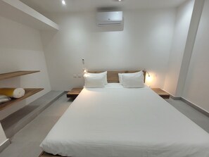 A modern hotel room with a large bed, wooden headboard, bedside tables, and a built-in air conditioning unit.