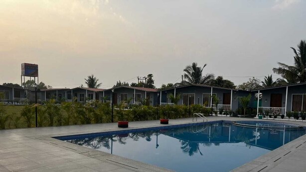 Une piscine dotée d’une terrasse carrelée, entourée de petits bâtiments et de palmiers.