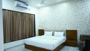 Une chambre à coucher avec un lit, des rideaux, un appareil de climatisation et un mur décoré d’un motif.
