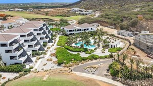 A resort with modern architecture, a pool area, and a golf course in the background. - Reef View - Ocean View | Modern Apartment (Blue Bay Golf &amp; Beach Resort)